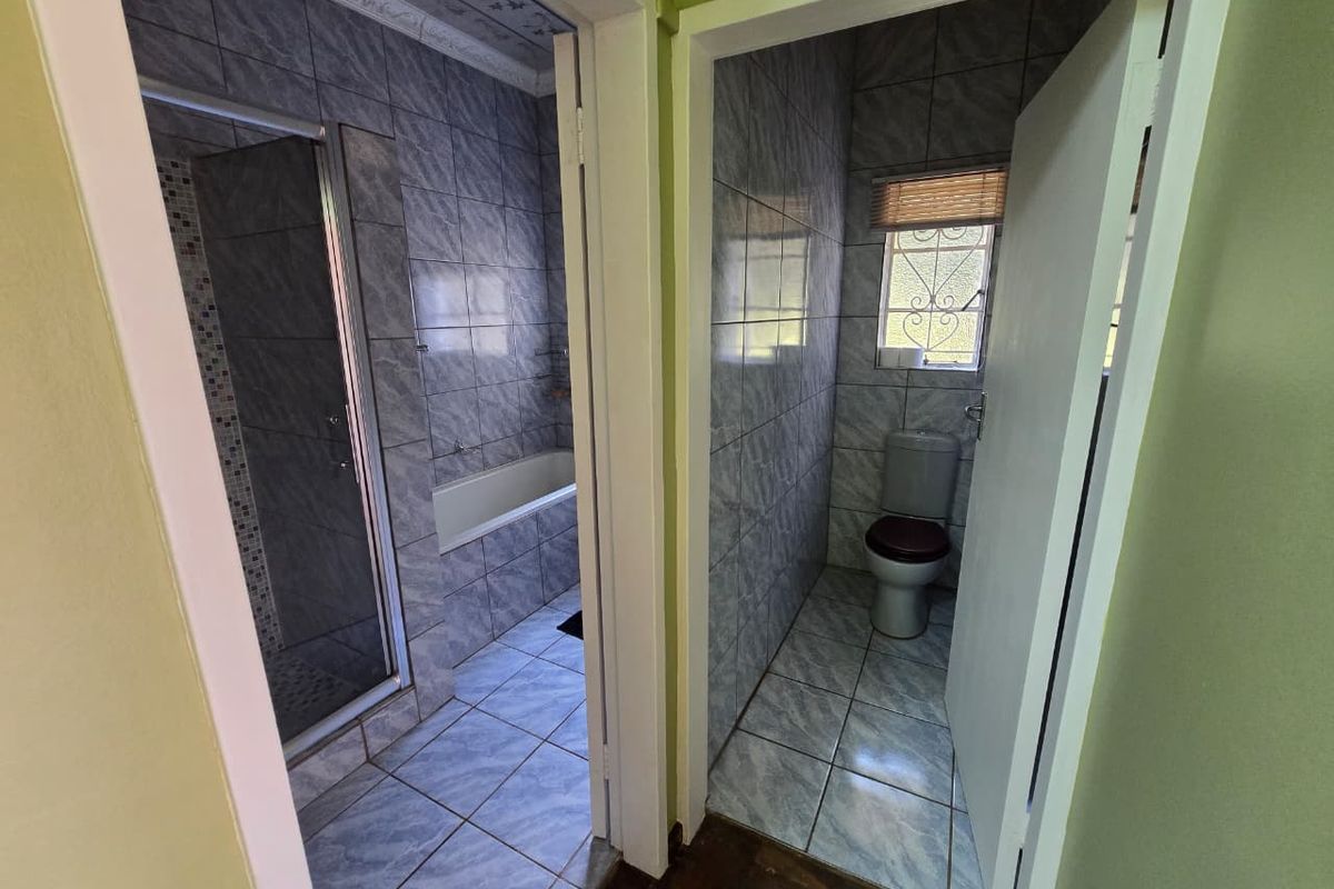 A functional bathroom layout featuring a separate shower and bathtub area alongside a private toilet cubicle with tiled finishes throughout.