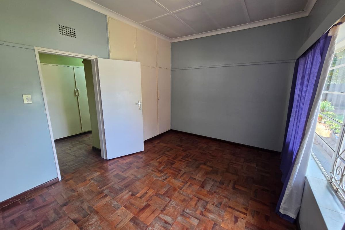 A bedroom featuring original parquet flooring, built-in cupboards, and a large window allowing natural light.