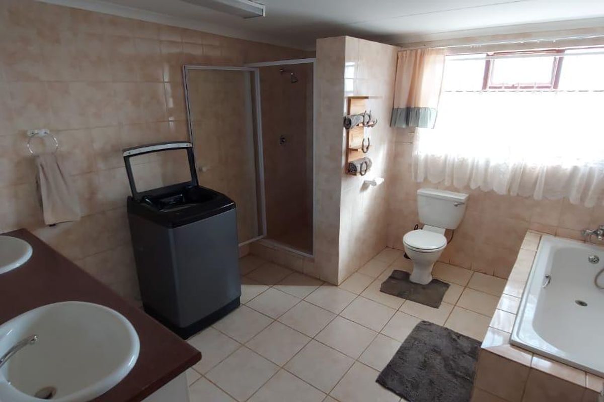 Spacious bathroom featuring a double vanity, a built-in bathtub, a separate shower enclosure, and a toilet, finished with neutral wall and floor tiles.