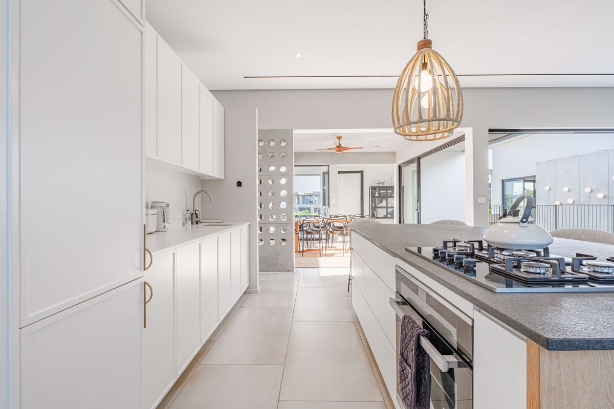 Modern, high-end kitchen featuring sleek white cabinetry, stone countertops, a central island with a gas cooktop, and integrated appliances in an open-plan layout.