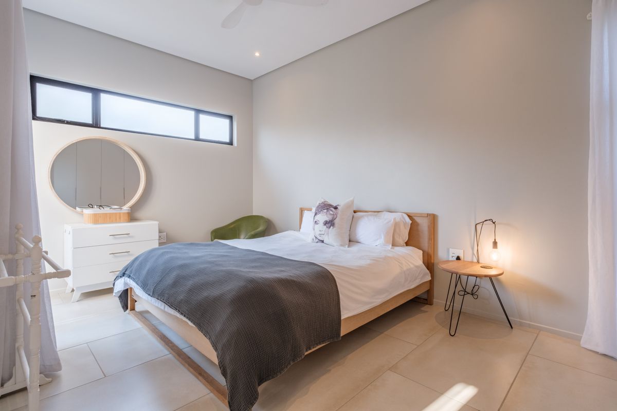 A bright and modern bedroom featuring large format floor tiles, a high ceiling with a fan, and a sleek clerestory window.