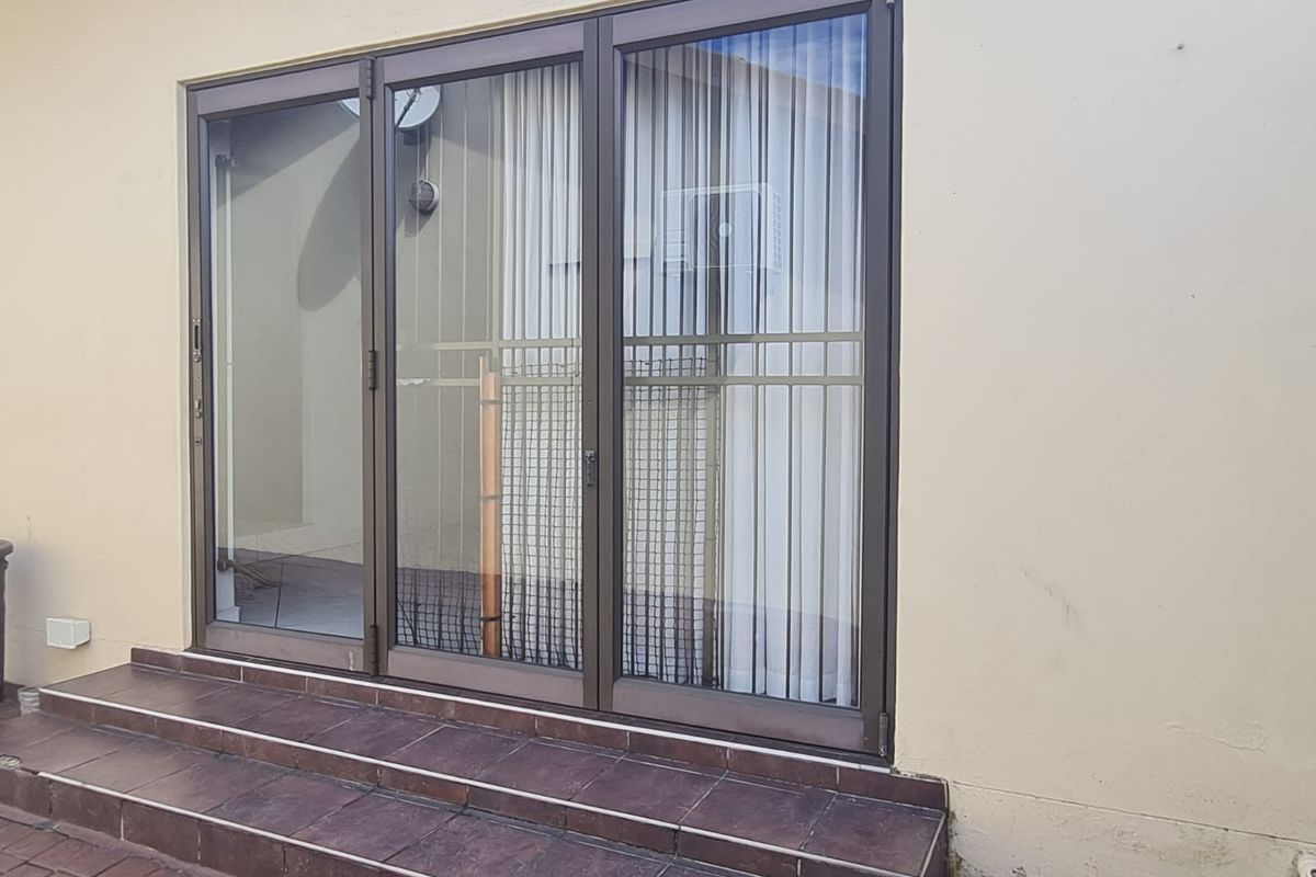 Exterior view of a rear entrance featuring dark-framed sliding glass doors with security bars and tiled steps leading to the patio area.
