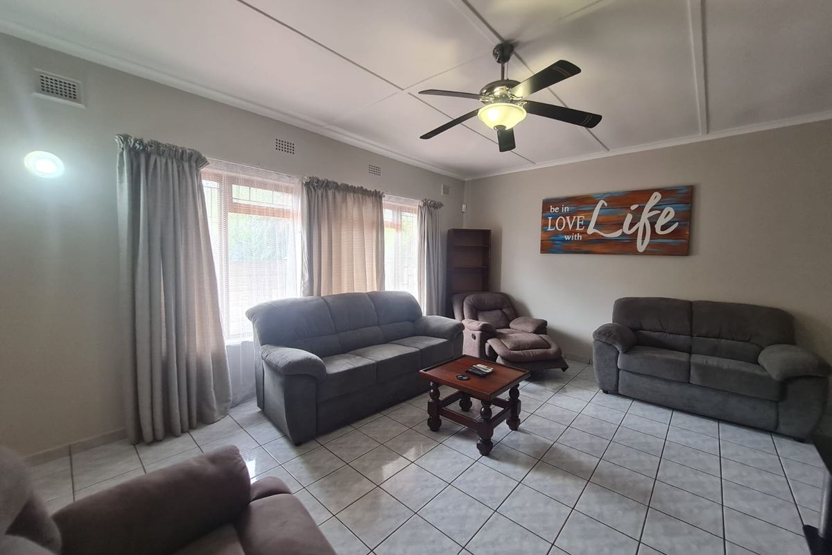 A spacious living room featuring tiled flooring, a ceiling fan, and large windows that provide ample natural light.