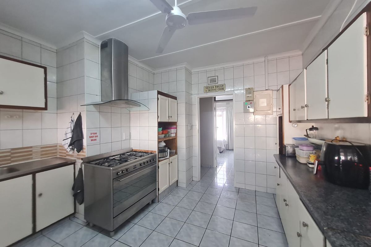 Functional kitchen featuring tiled walls and flooring, stainless steel gas stove with extractor fan, and ample built-in cabinetry.