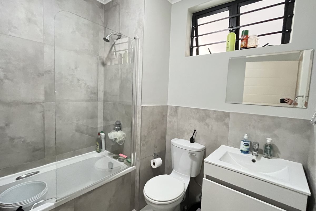 Modern bathroom featuring a shower-over-bath combination with glass screen, wall-mounted vanity, and neutral grey tiling throughout.