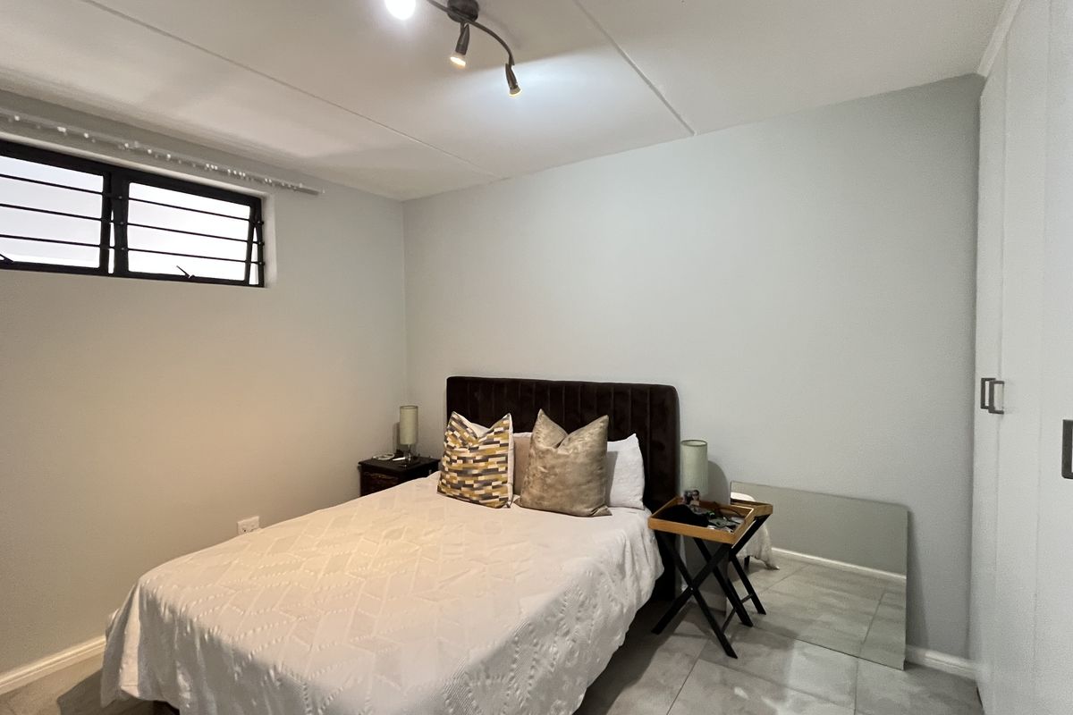 A bedroom featuring tiled flooring, built-in wardrobes, and a window with security bars, providing a functional and neutral living space.