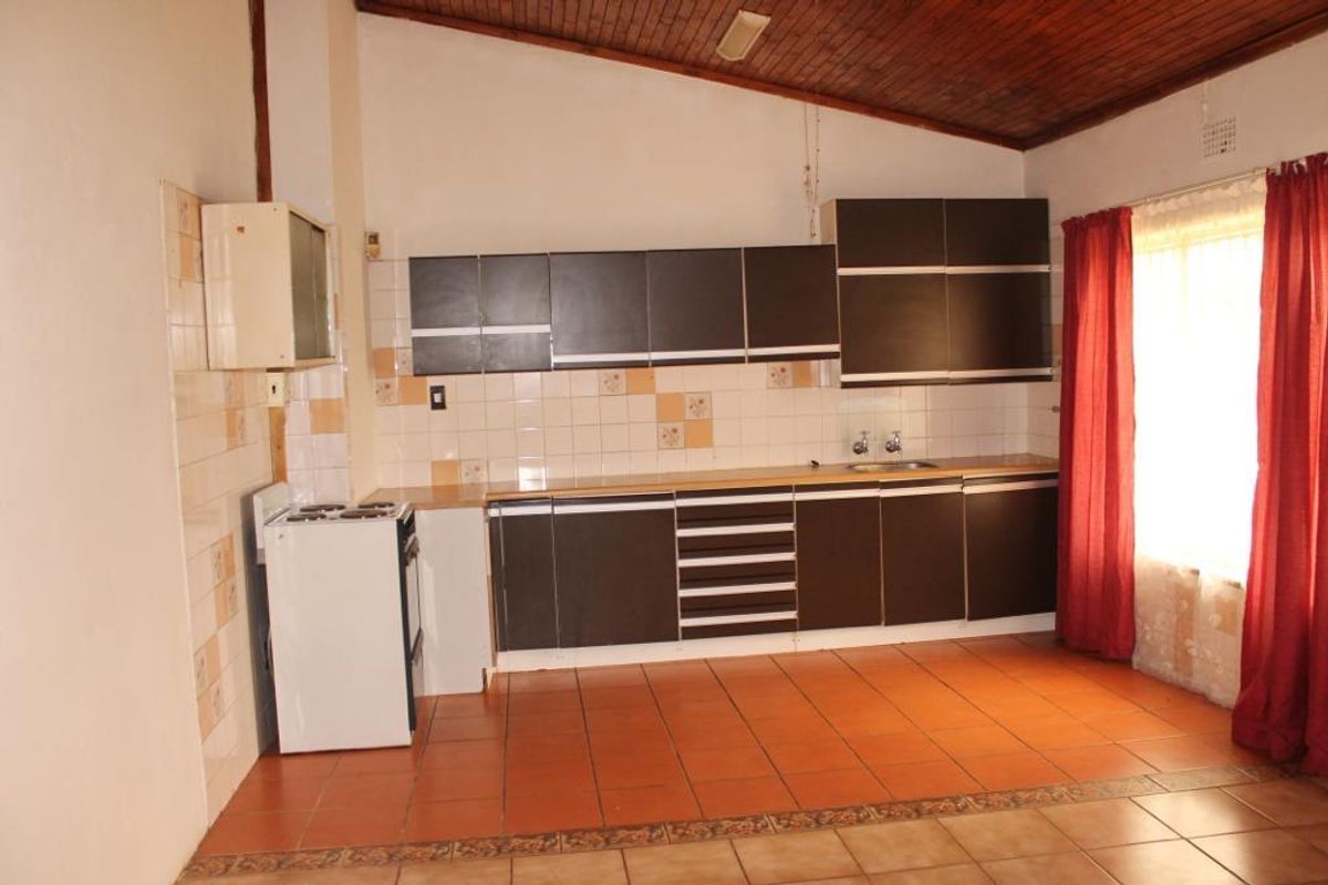 A functional kitchen featuring dark cabinetry, tiled flooring, and a timber-paneled ceiling, offering a practical layout with ample storage space.