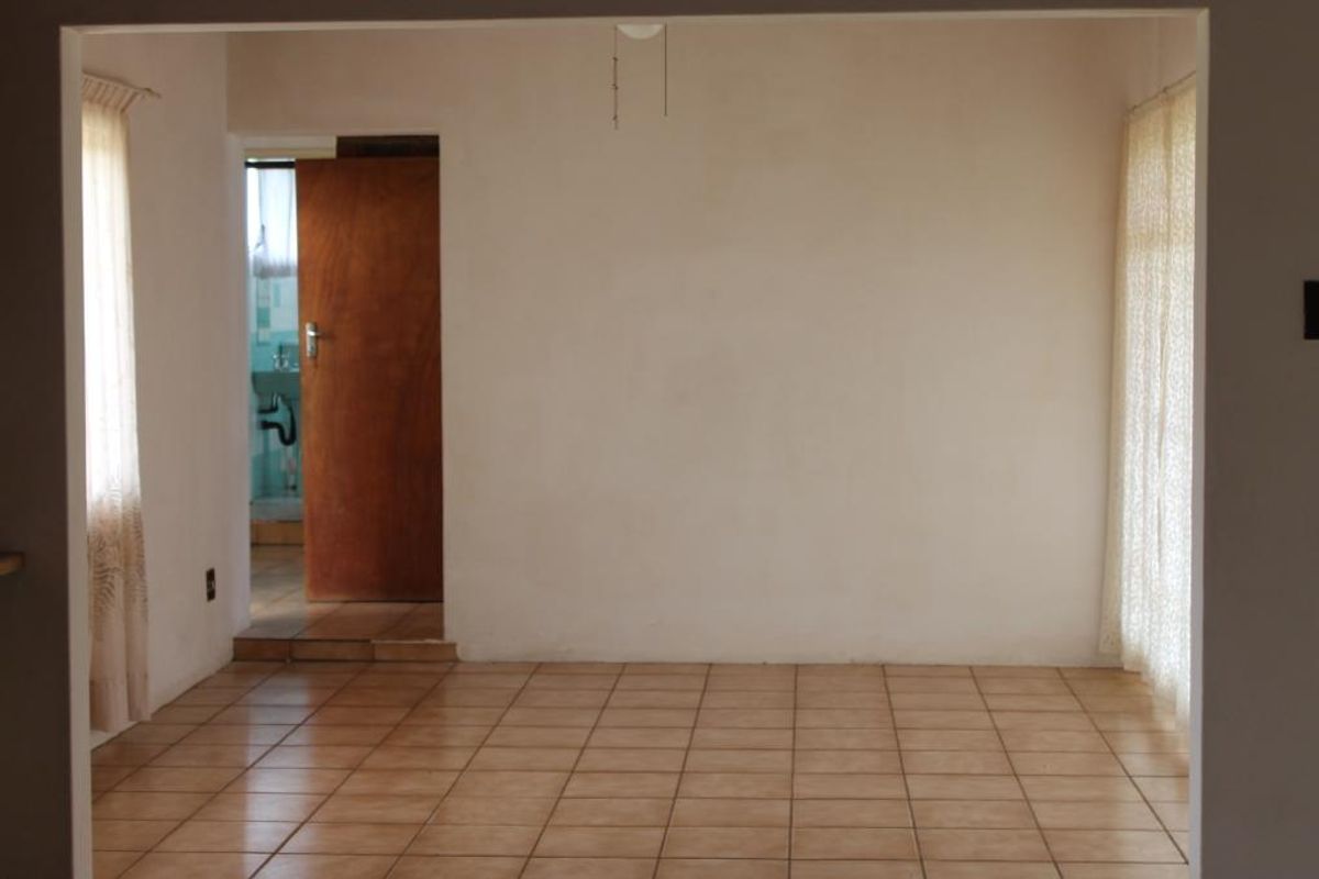 An empty living area featuring ceramic floor tiles, neutral wall finishes, and direct access to an adjacent bathroom space.