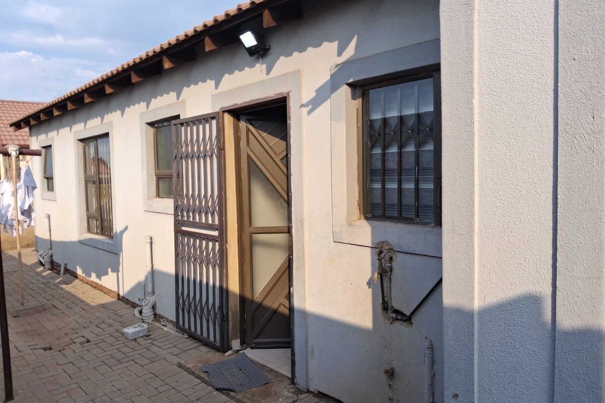 Exterior view of the rear building elevation featuring a paved walkway, security gates, and external wall-mounted lighting.