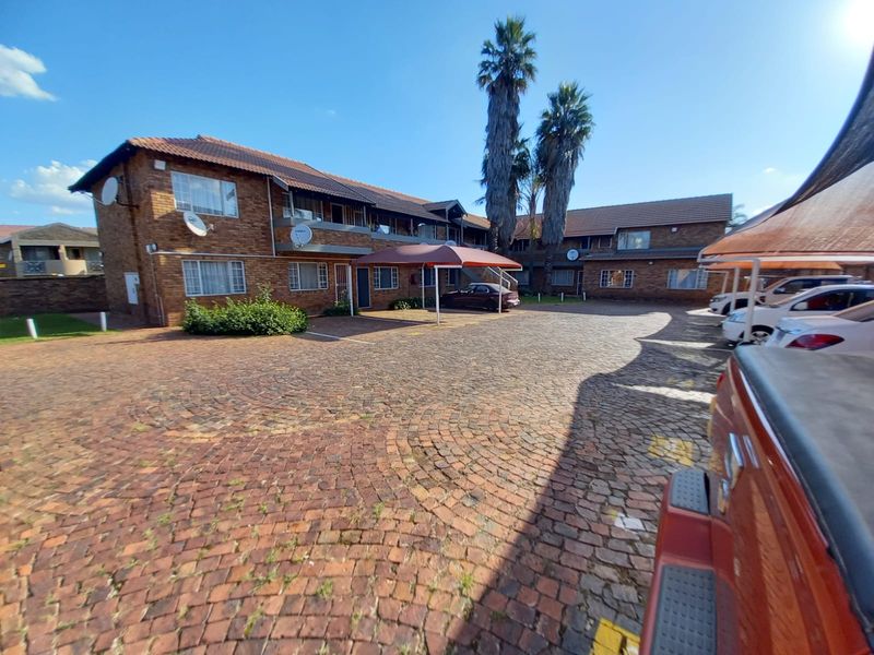 Exterior view of a brick apartment complex featuring a paved courtyard, covered parking bays, and established landscaping.