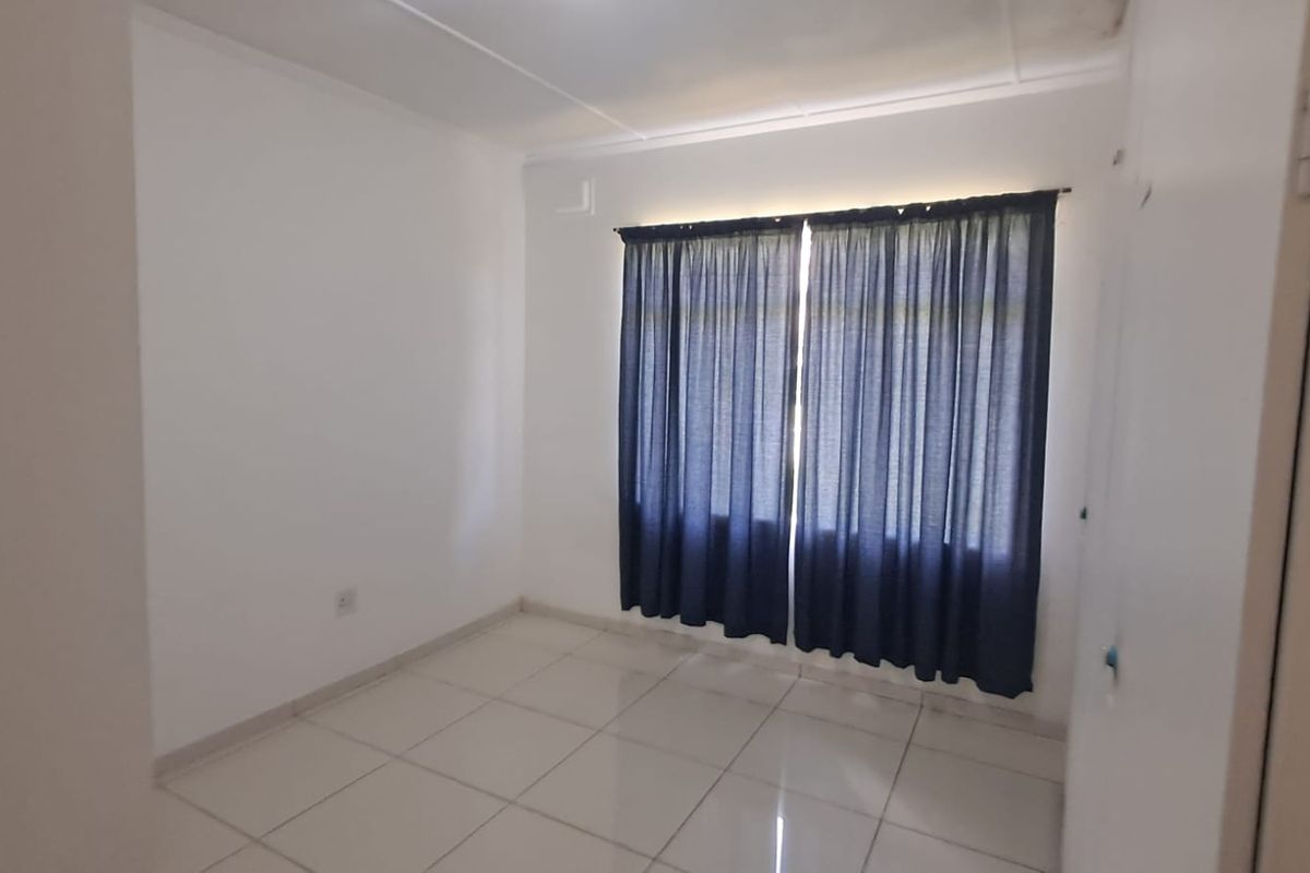A bright, empty bedroom featuring neutral tiled flooring and a large window dressed with dark blue curtains.