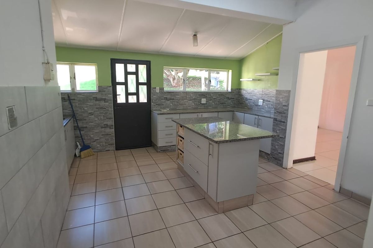 A functional kitchen featuring a central island, stone-look countertops, tiled splashbacks, and tiled flooring, providing a practical workspace with direct outdoor access.