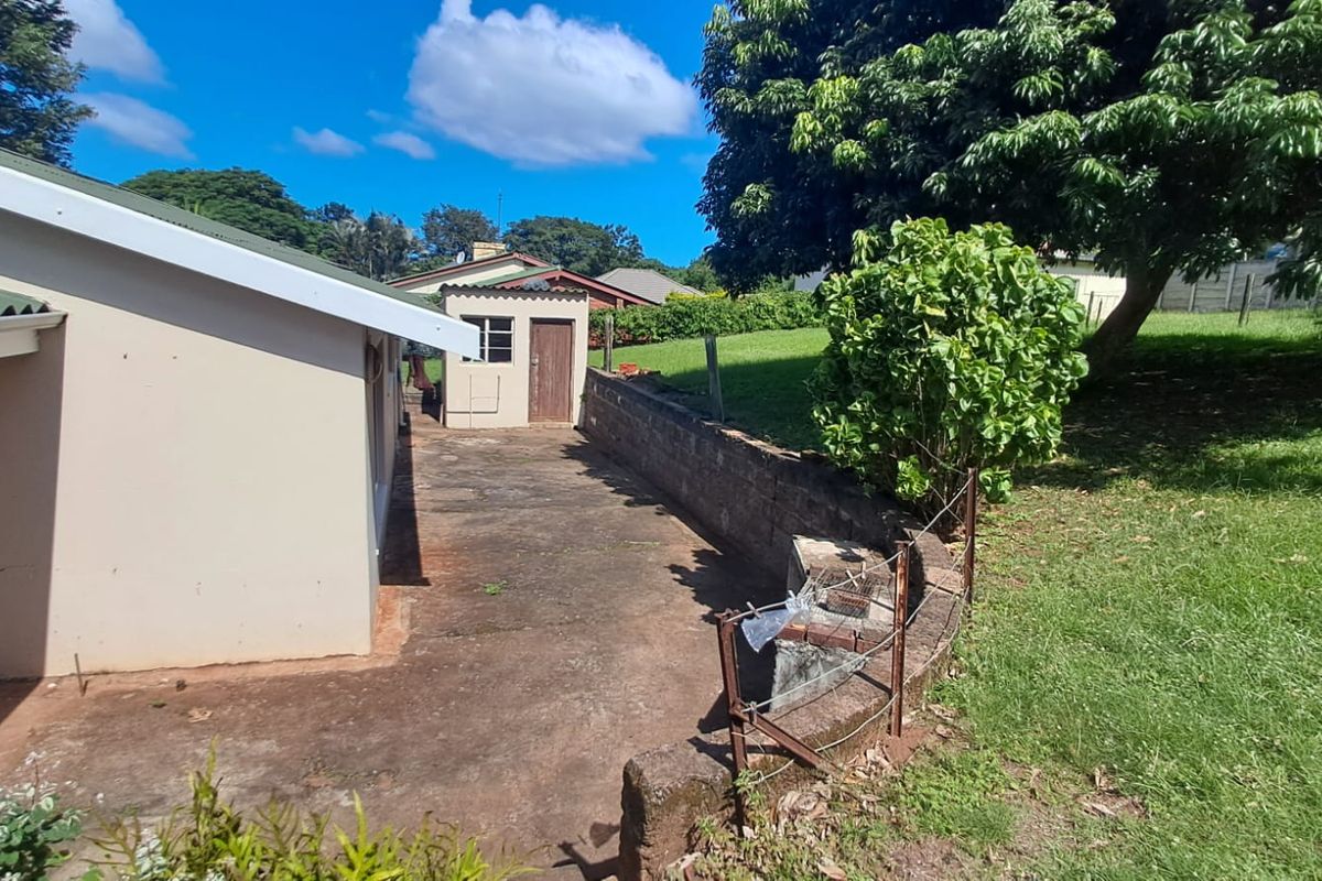 A view of the rear exterior area featuring a concrete patio, a small detached utility structure, and a grassed garden with a retaining wall.