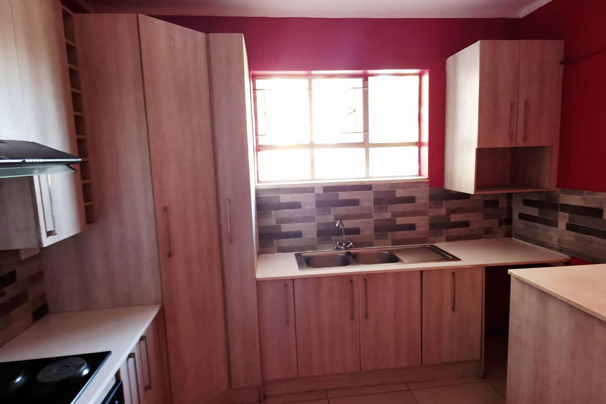 A functional kitchen featuring light wood-look cabinetry, laminate countertops, a double bowl sink, and a built-in electric hob with an extractor fan.