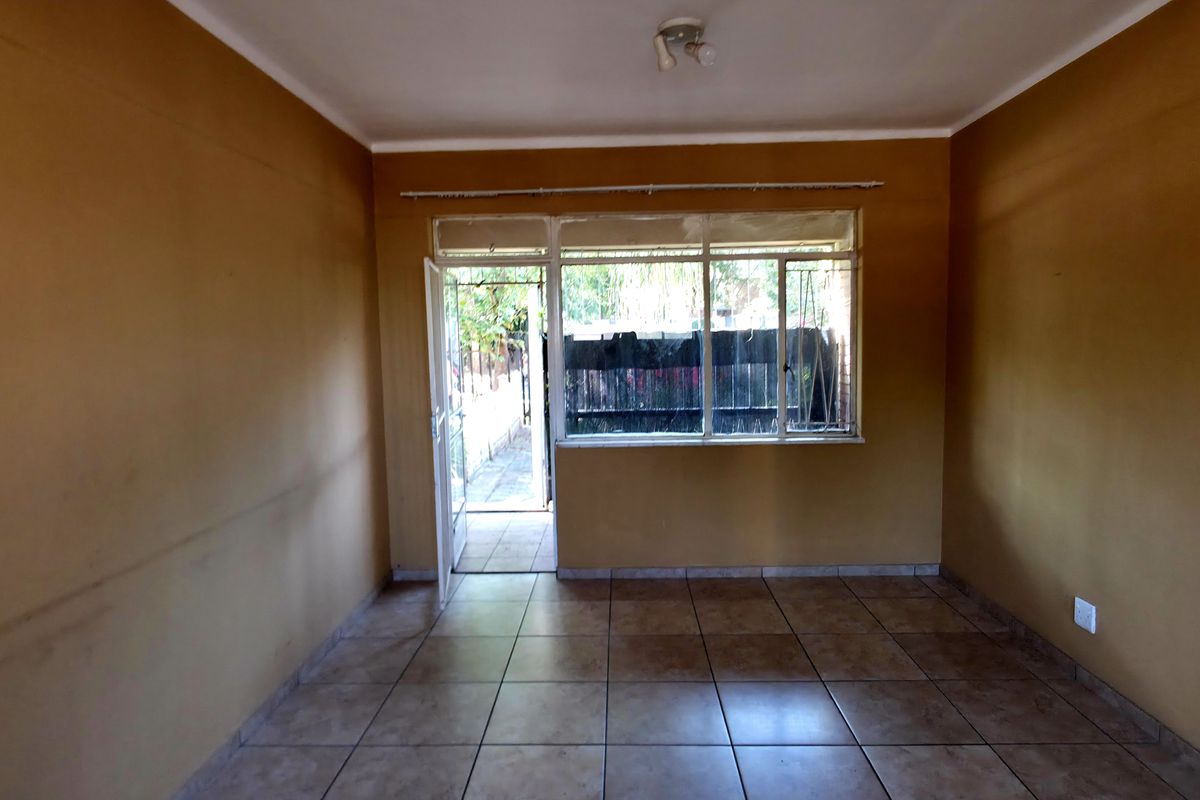 An empty living room featuring tiled flooring, large windows, and a glass door leading to an outdoor area.