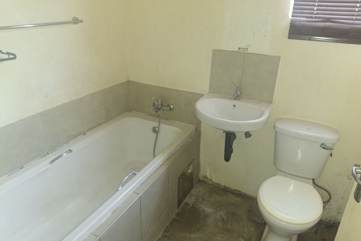 A dated bathroom featuring a standard bathtub, pedestal sink, and toilet, requiring significant cosmetic updates and floor repairs.