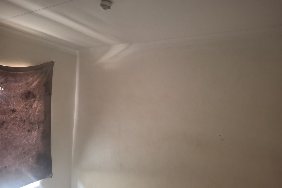 A view of a bedroom interior featuring plain walls, a ceiling light fixture, and a window.