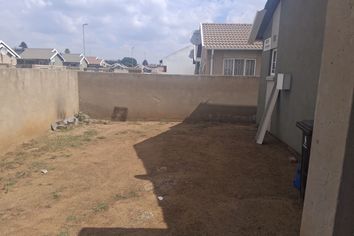 A rear exterior view of the property featuring a private yard area enclosed by a perimeter wall.