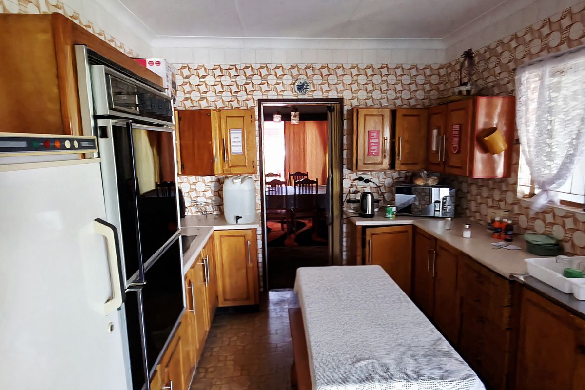 A dated kitchen featuring wooden cabinetry, integrated wall oven, and patterned wall tiles, offering a functional layout with potential for modernization.