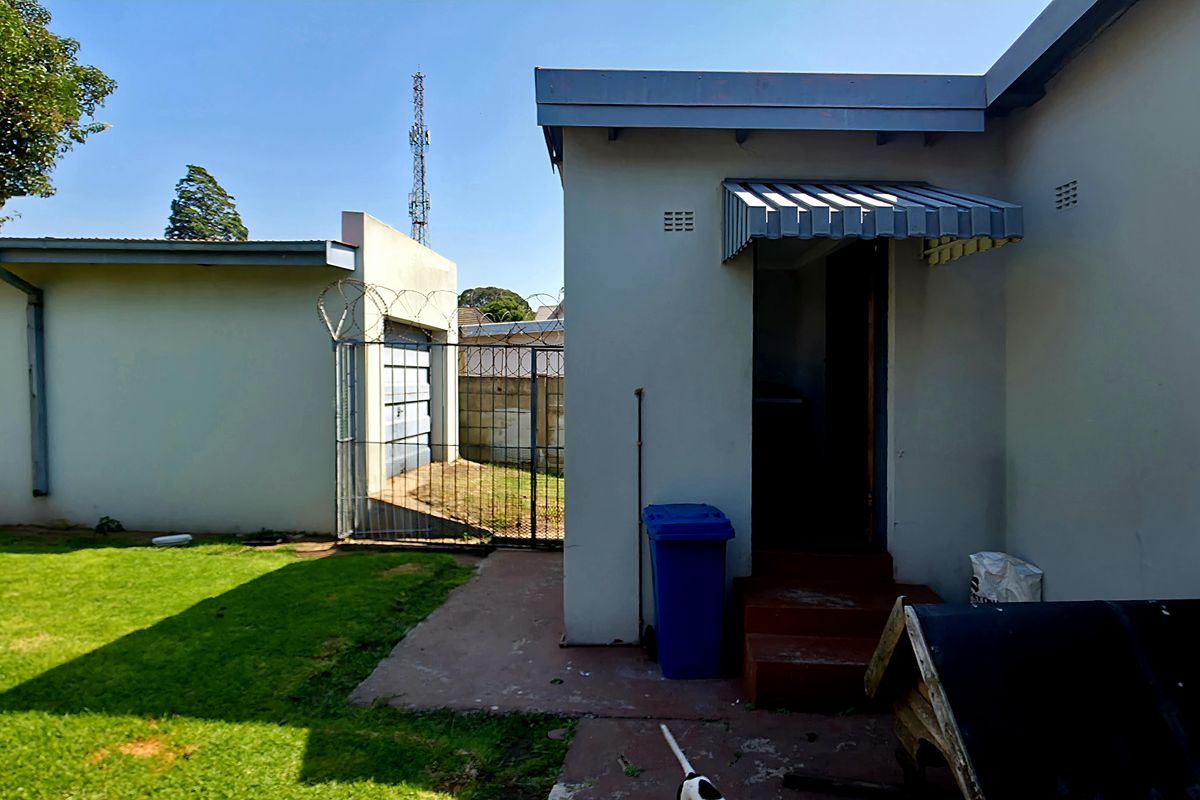 Rear exterior view of the property featuring a small lawn, concrete pathway, and access to the rear entrance with a metal awning.