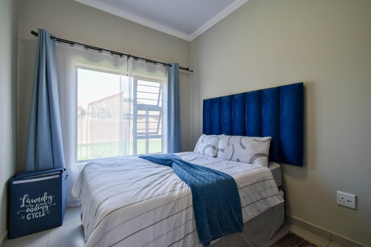 A well-maintained bedroom featuring neutral wall tones, tiled flooring, and a large window that provides natural light.