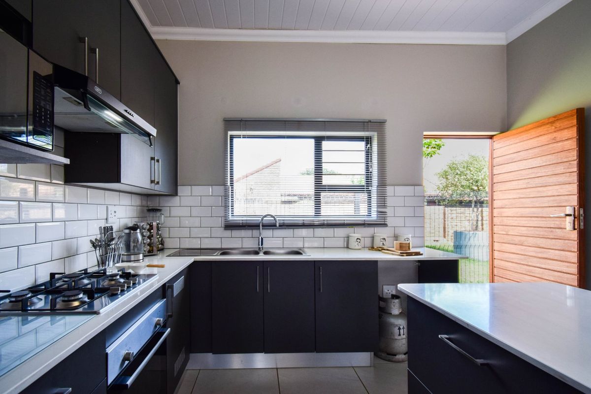 Modern kitchen featuring dark cabinetry, white subway tile backsplash, stone countertops, built-in gas hob, oven, and extractor fan with direct access to the garden.