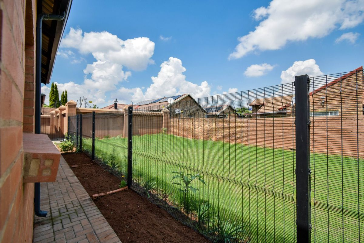 A well-maintained rear garden featuring a manicured lawn, paved walkway, and secure perimeter wire mesh fencing.