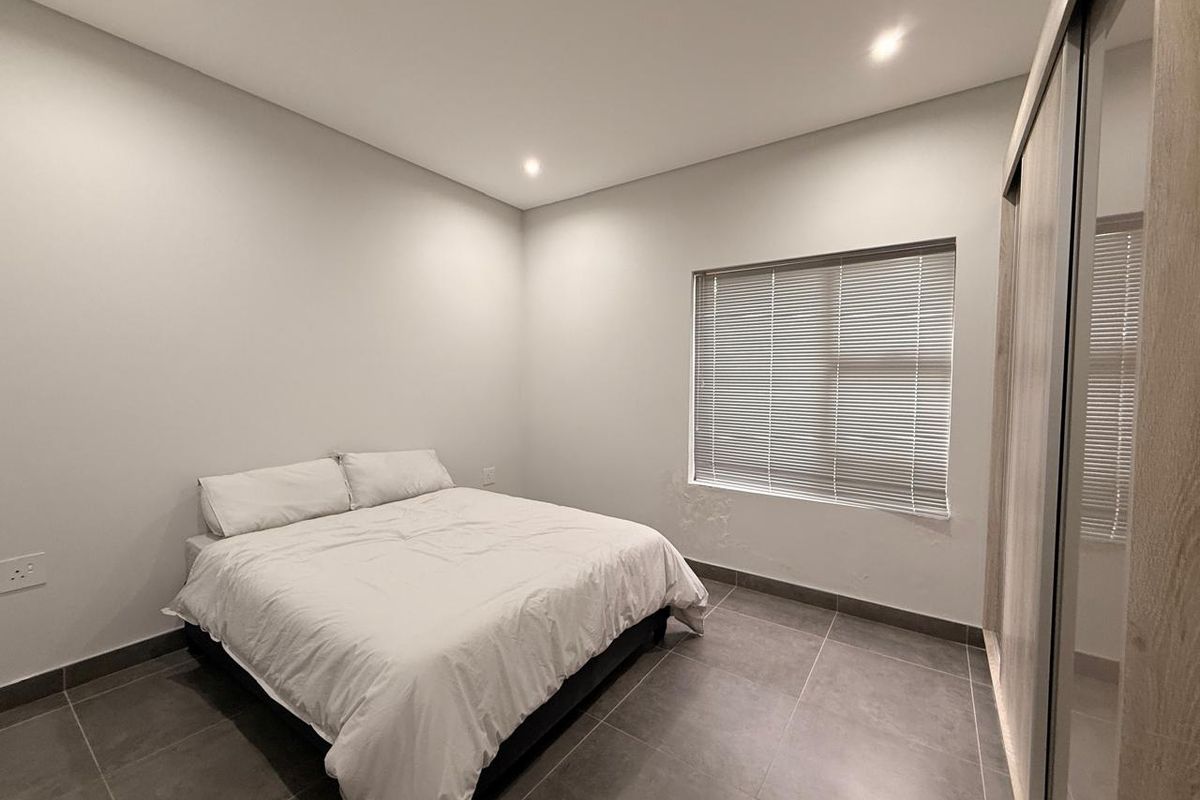 A modern bedroom featuring tiled flooring, recessed ceiling lighting, a built-in sliding door wardrobe, and a window with fitted blinds.