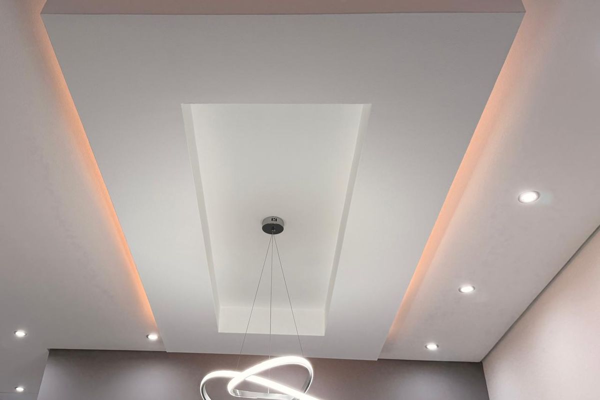A modern interior ceiling featuring a recessed tray design with integrated ambient cove lighting and recessed downlights.