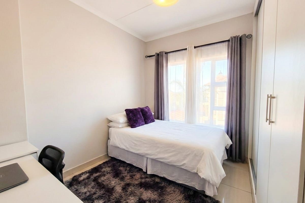 A bright bedroom featuring tiled flooring, built-in sliding door wardrobes, and large windows that provide natural light.