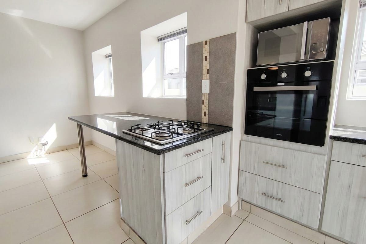 Modern kitchen featuring light wood-grain cabinetry, granite countertops, a built-in oven, microwave, and a gas hob with a tiled splashback.