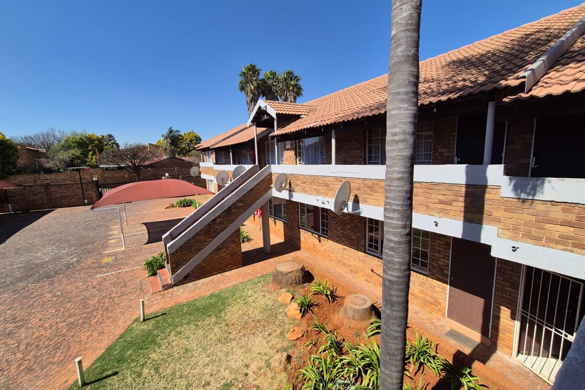 Exterior view of a multi-story apartment complex featuring face-brick facade, tiled roofing, external staircases, and paved courtyard area.