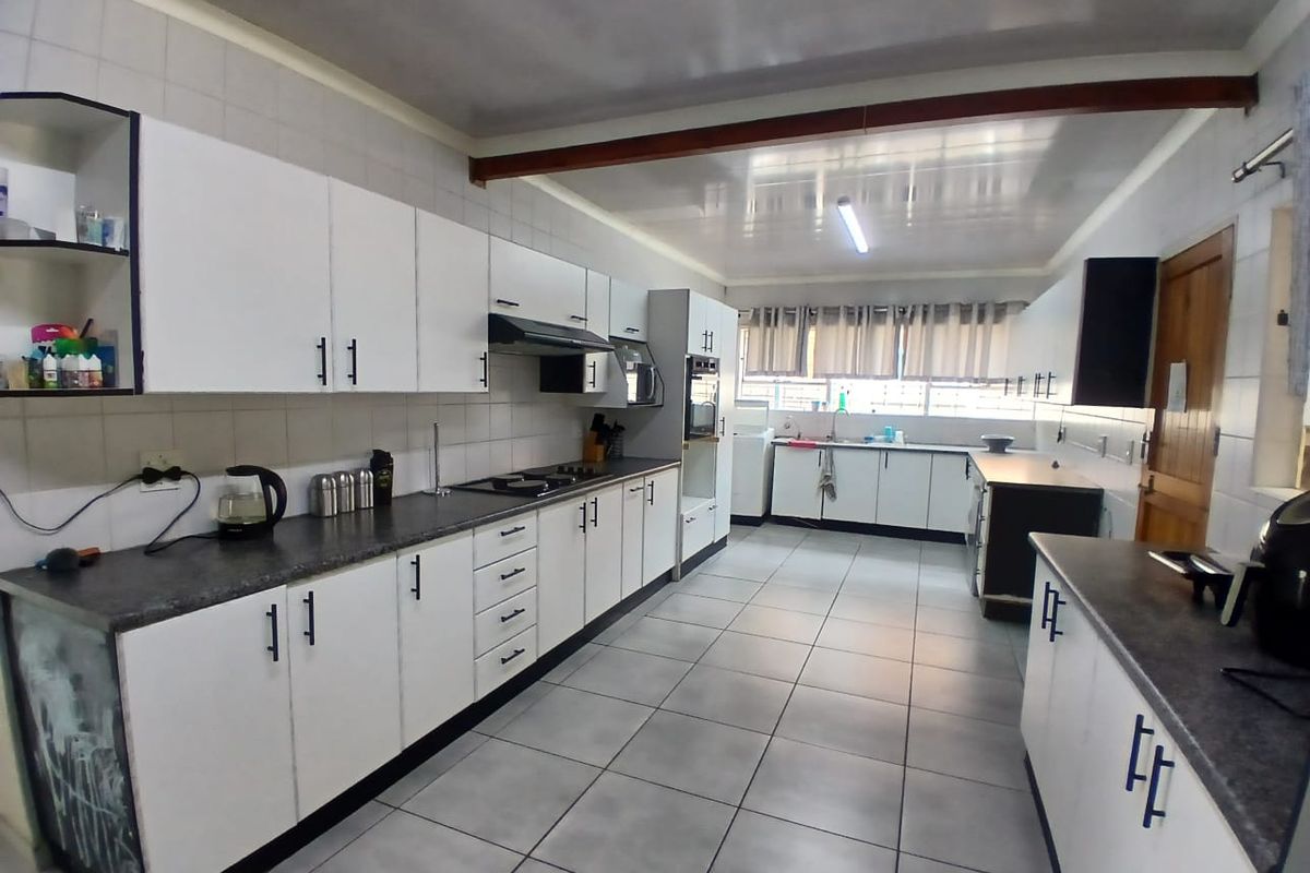 Spacious kitchen featuring extensive white cabinetry, dark laminate countertops, built-in oven, extractor fan, and tiled flooring throughout.