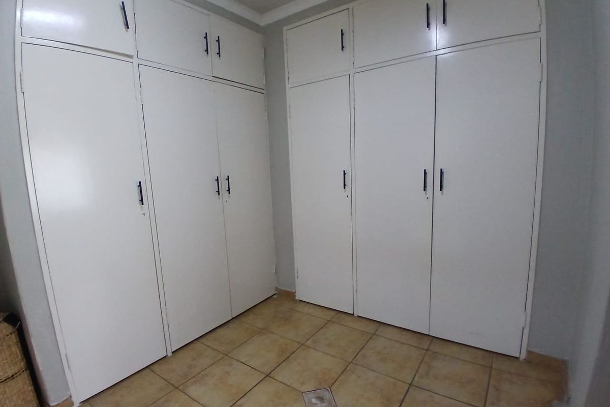 A bedroom featuring extensive white built-in cupboards and neutral tiled flooring, offering ample storage space in a clean, functional layout.