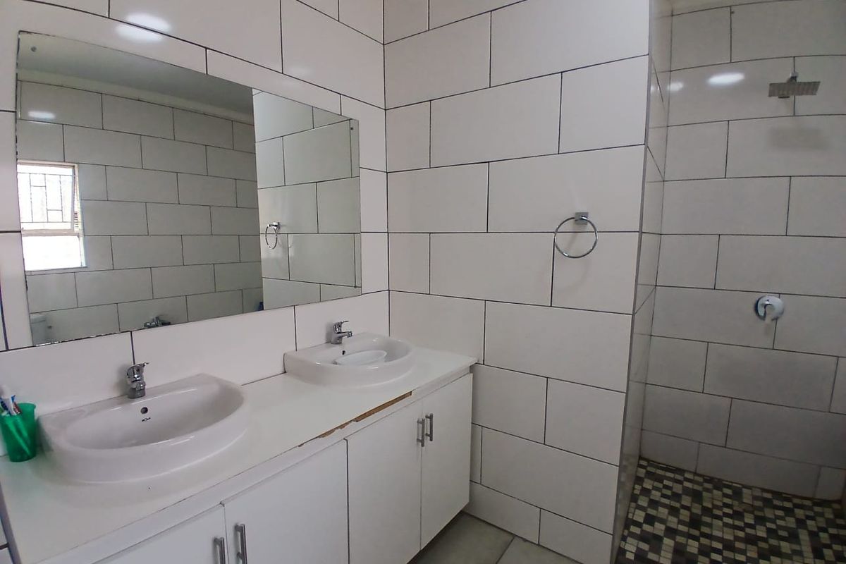 Modern bathroom featuring a double vanity with built-in cabinetry, a large wall-mounted mirror, and a spacious walk-in shower with a rainfall shower head.