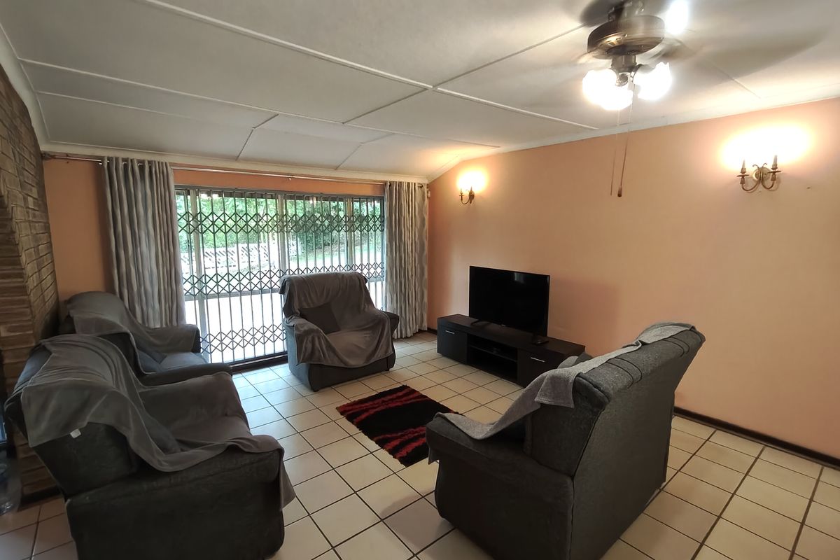 A living room featuring tiled flooring, a brick feature wall, ceiling fan, and large sliding doors with security gates leading to the exterior.