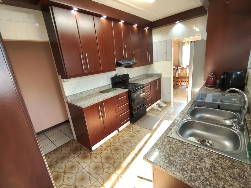 A functional kitchen featuring dark wood cabinetry, granite-look laminate countertops, a double stainless steel sink, and a freestanding stove with an extractor fan.