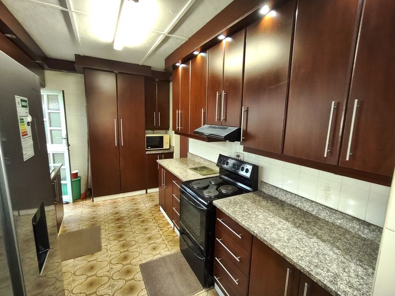 A functional kitchen featuring dark wood cabinetry, granite countertops, and an electric stove with an integrated extractor fan.