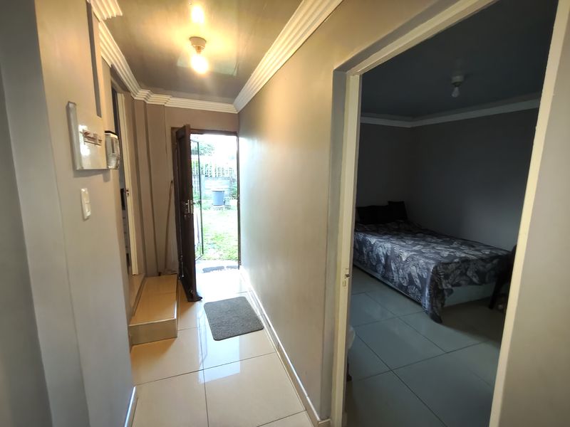 A functional hallway featuring tiled flooring and crown molding, providing access to an adjacent bedroom and an exterior entrance.