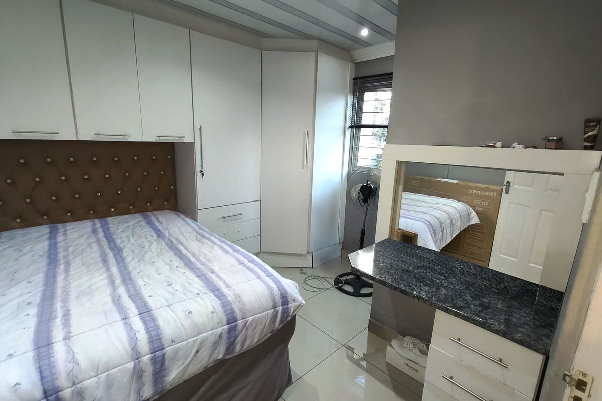 A well-maintained bedroom featuring extensive white built-in cupboards, a matching built-in vanity unit, and neutral tiled flooring.