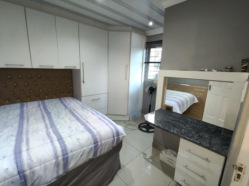 A well-maintained bedroom featuring extensive white built-in cupboards, a matching built-in vanity unit, and neutral tiled flooring.