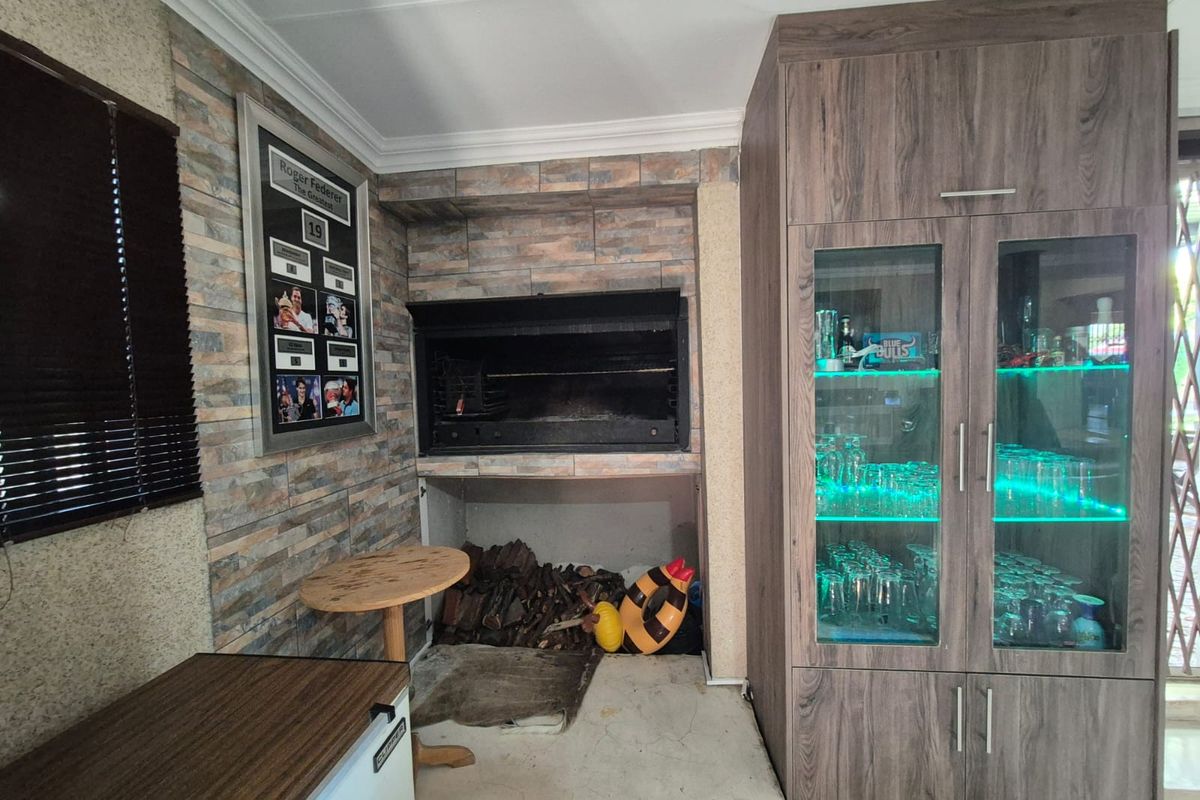 Indoor entertainment area featuring a built-in braai with stone-cladding surround and custom cabinetry with integrated glass display shelving.