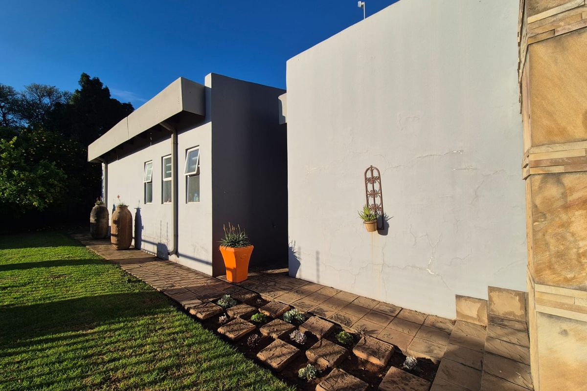 A view of the rear exterior facade featuring paved pathways, manicured lawn, and stone-clad architectural detailing.