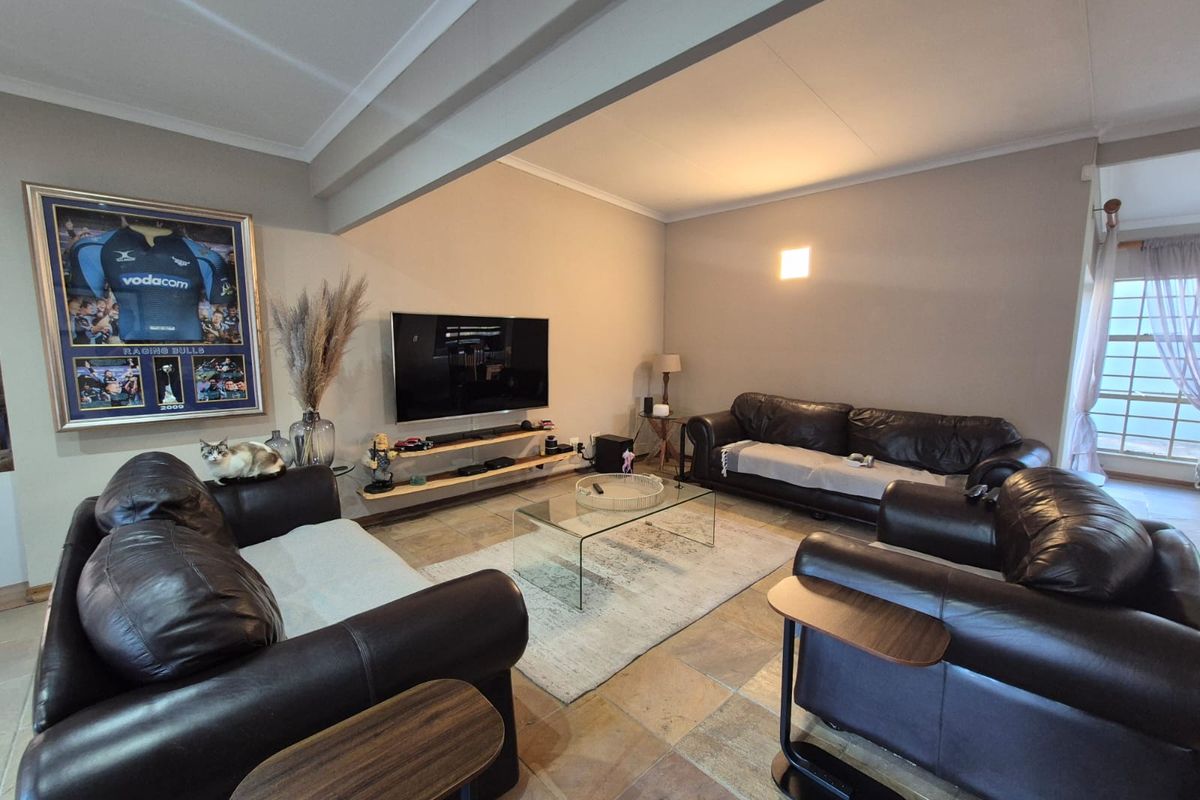 A spacious living room featuring natural stone tile flooring, neutral wall tones, and a wall-mounted television setup.