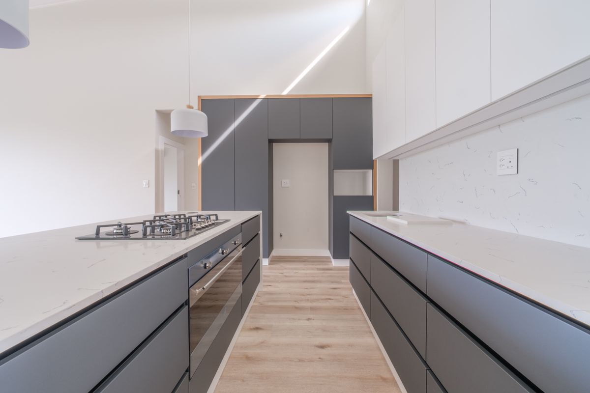 Modern kitchen featuring sleek grey cabinetry, stone countertops, a central island with a gas cooktop, and high-quality laminate flooring in a bright, open space.