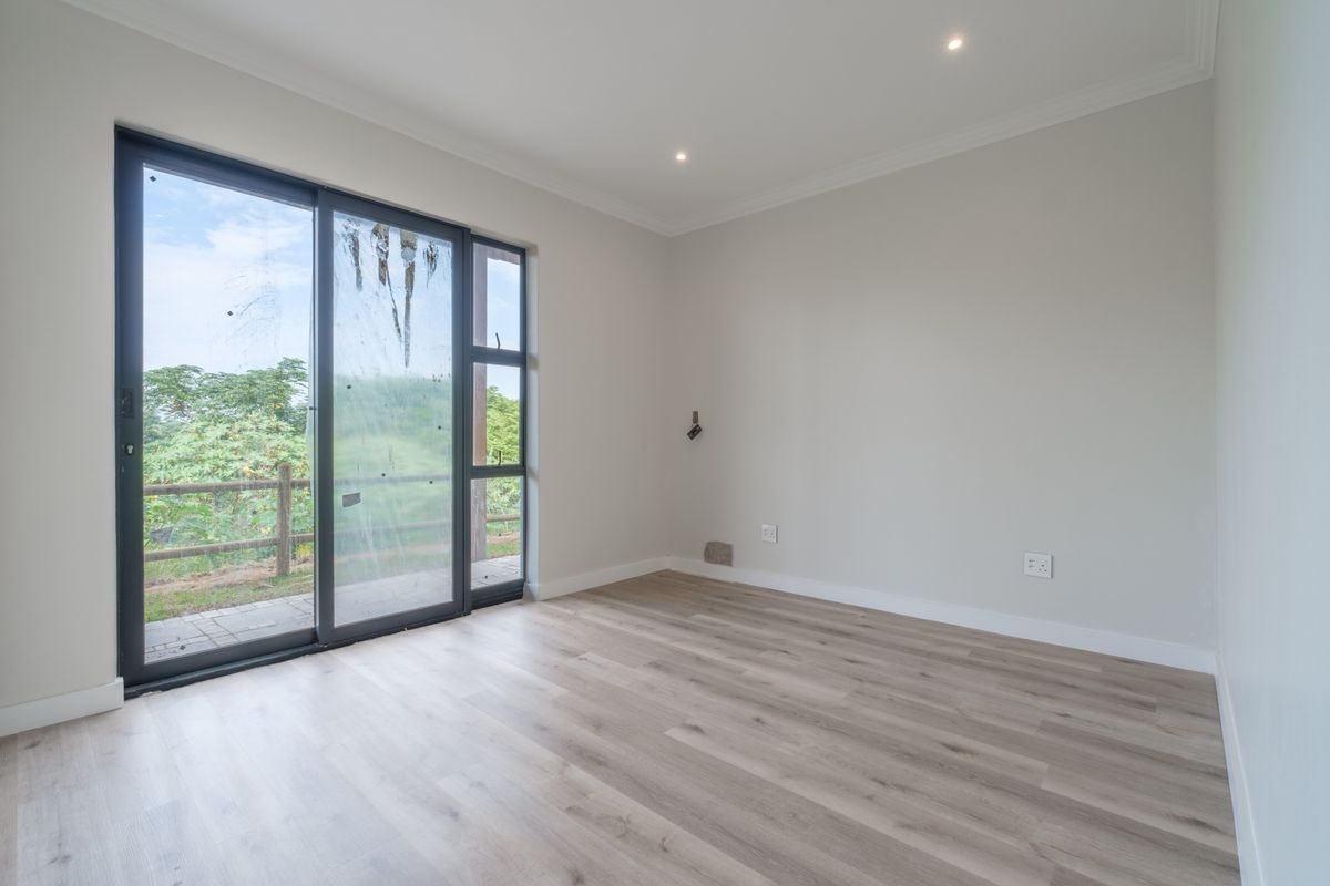 A bright, empty bedroom featuring modern laminate flooring, recessed lighting, and a large sliding glass door providing access to the outdoor area.