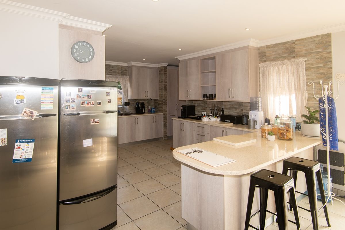A functional kitchen featuring light wood-grain cabinetry, stone-look countertops, a breakfast bar, and tiled flooring throughout.