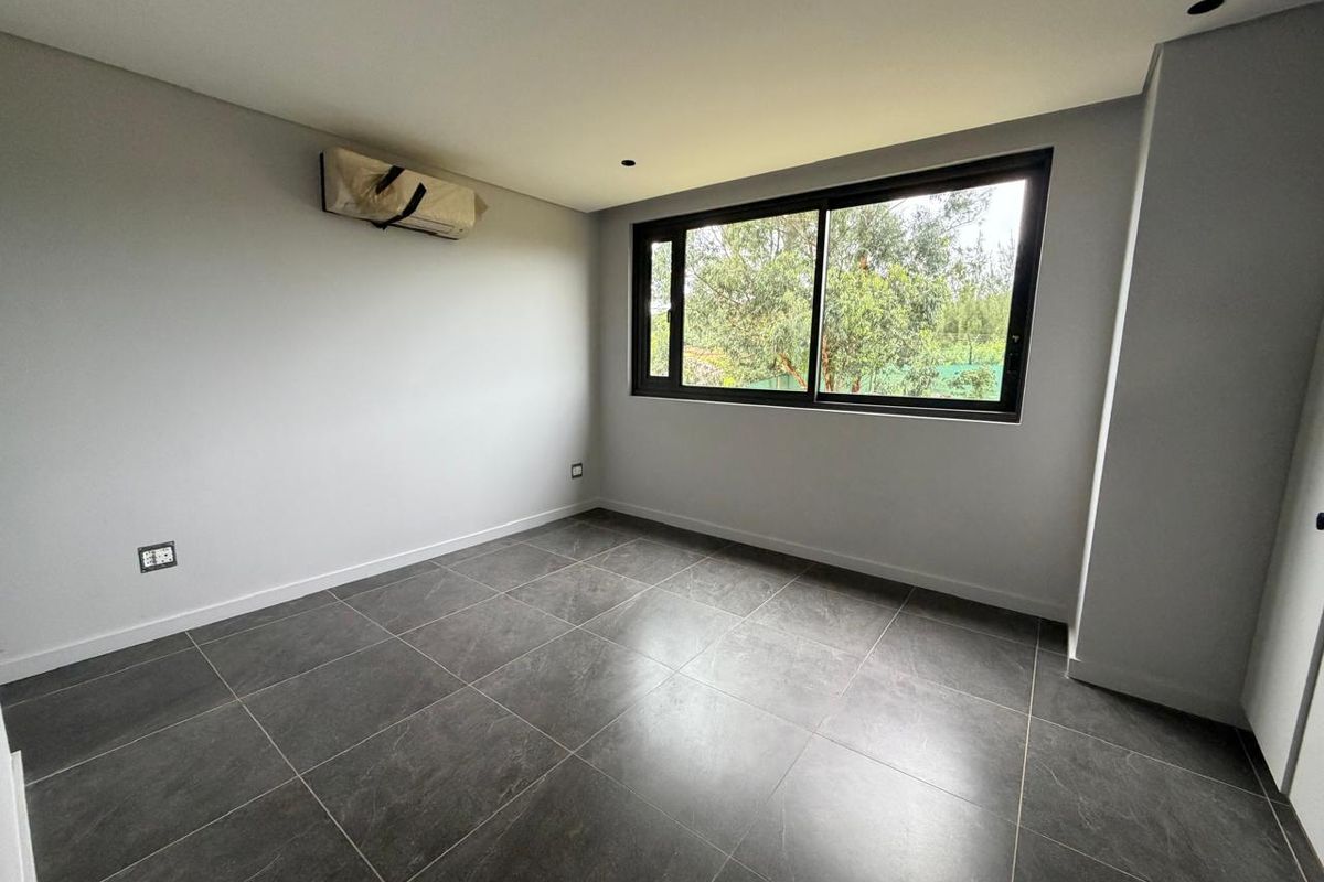 A bright, empty bedroom featuring modern dark floor tiles, recessed ceiling lighting, and a wall-mounted air conditioning unit.