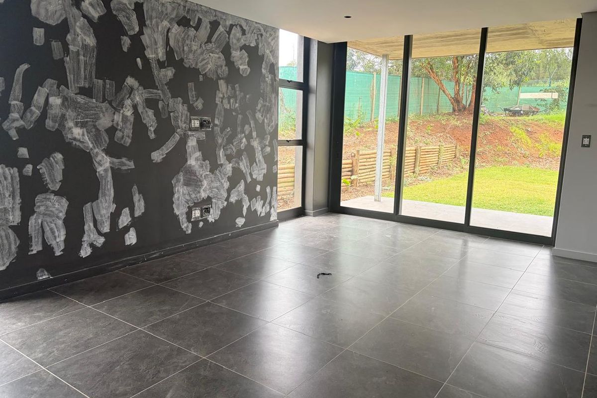 An empty living area featuring large floor-to-ceiling sliding glass doors, dark floor tiles, and a feature wall requiring finishing or repair.