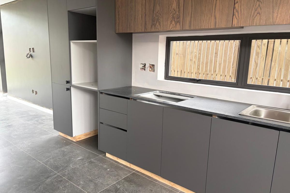 Modern kitchen featuring dark grey cabinetry, wood-grain upper cabinets, stone countertops, and dual stainless steel sinks, currently in the final stages of installation.
